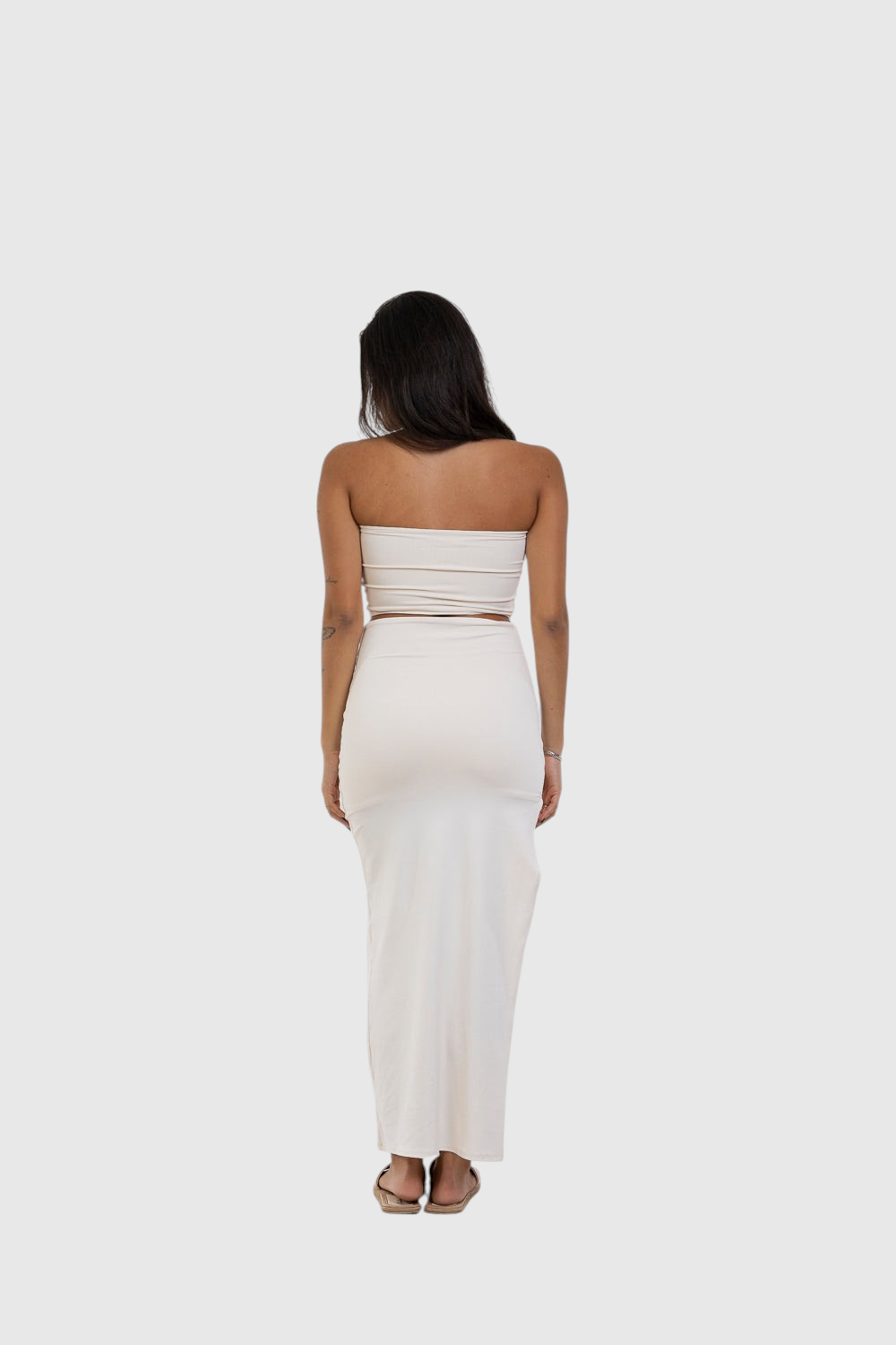 Modelo de costas vestindo saia midi off-white LA MAGIE com fenda, em poliamida justa que modela o corpo.