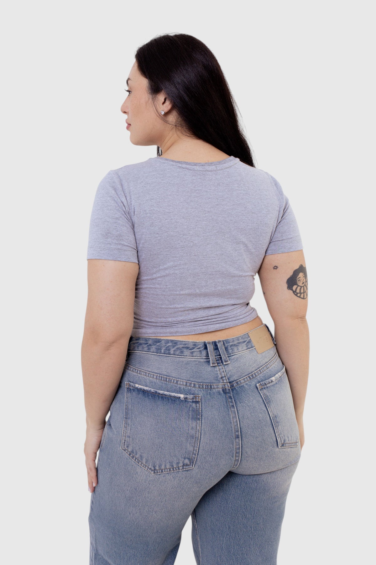 Modelo vestindo baby tee cinza de algodão da LA MAGIE | Roupas Femininas Básicas e Estilosas, vista de costas.
