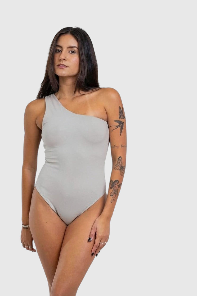 Modelo vestindo body LA MAGIE Nula Manga cinza de um ombro só em poliamida com forro duplo e toque macio.