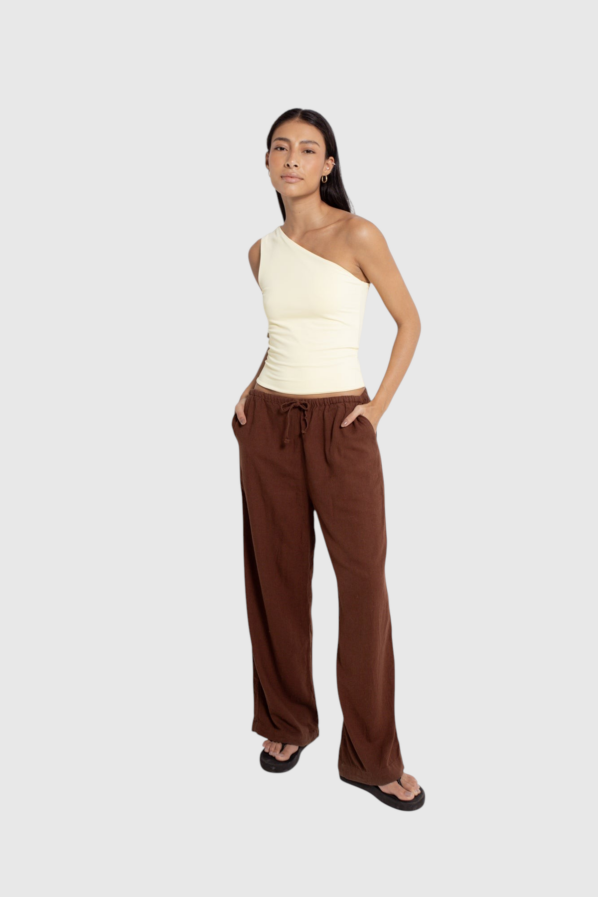 Modelo veste calça de linho marrom LA MAGIE com corte amplo, cintura ajustável por cordão e bolsos laterais.
