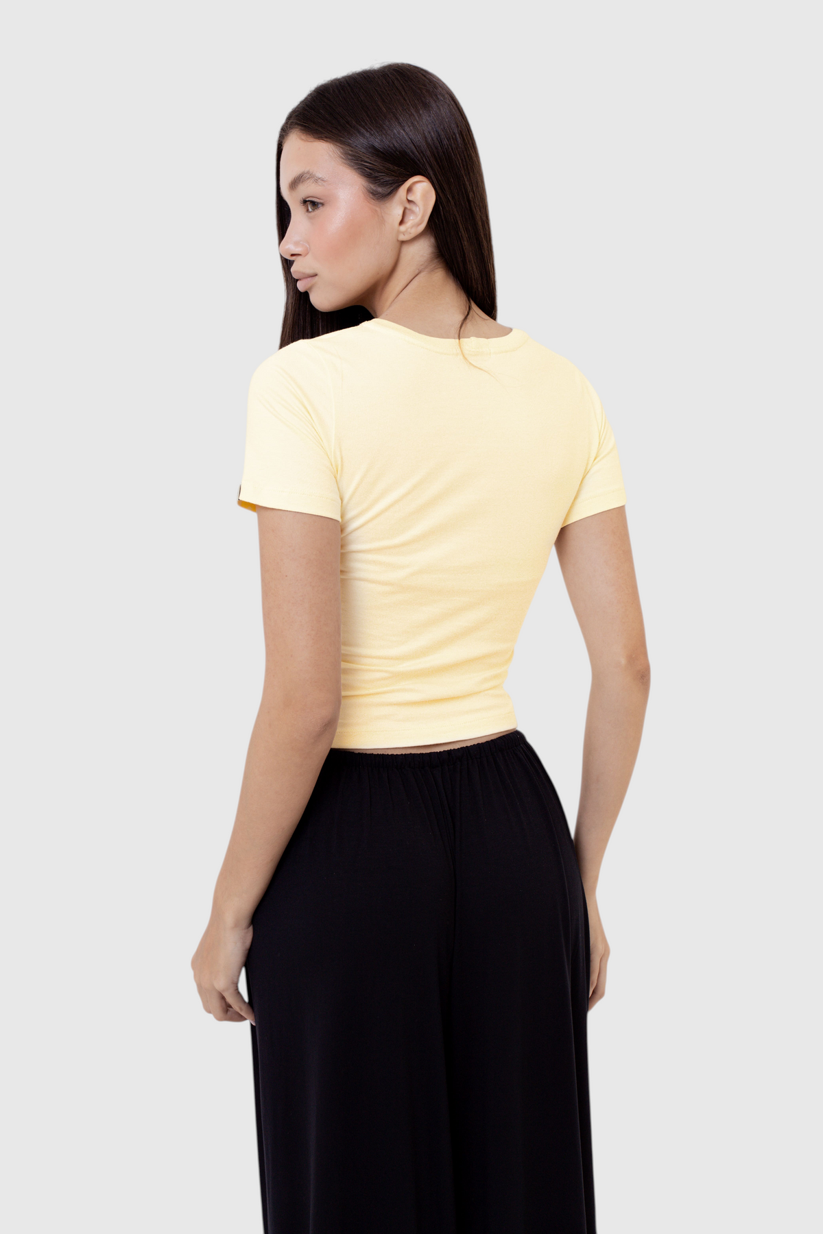 Modelo vestindo baby tee amarela de algodão da LA MAGIE | Roupas Femininas Básicas e Estilosas, vista de costas.