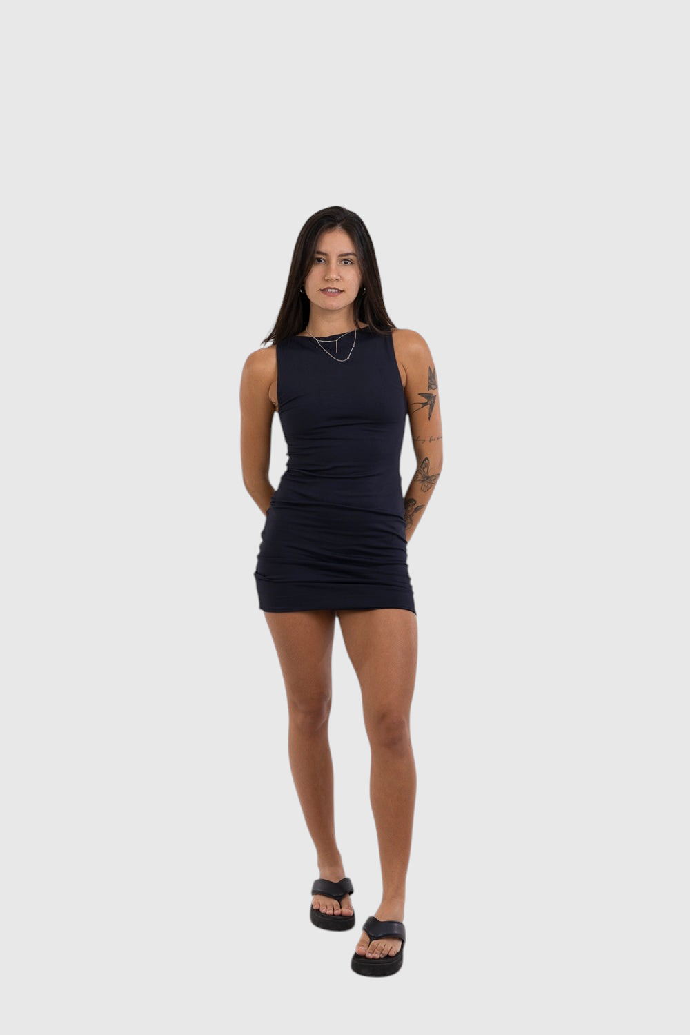 Modelo veste vestido curto preto LA MAGIE em poliamida com decote canoa e caimento ajustado ao corpo.