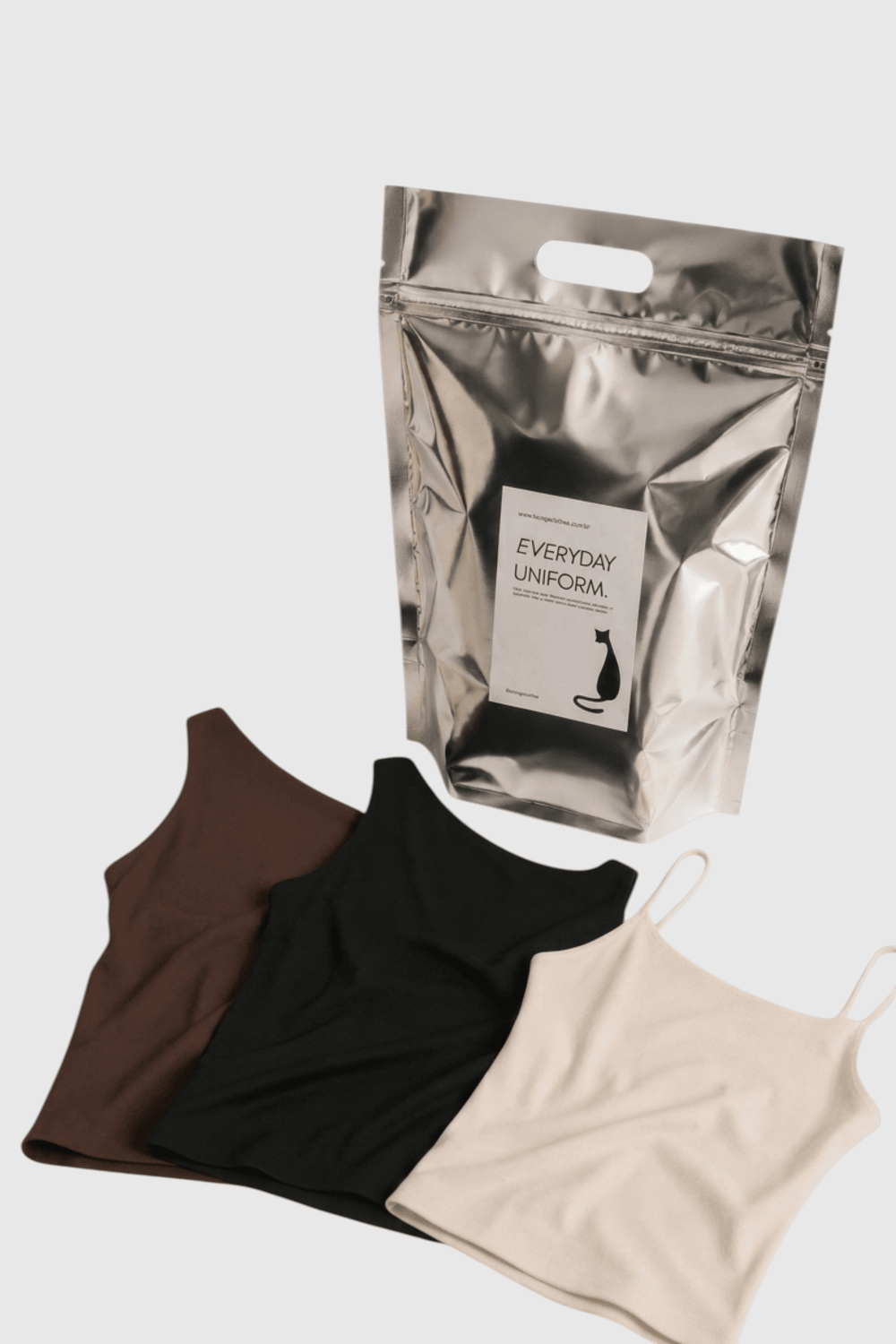 Kit Trio Essencial LA MAGIE com blusas em poliamida nas cores marrom, preta e off white em embalagem metalizada.