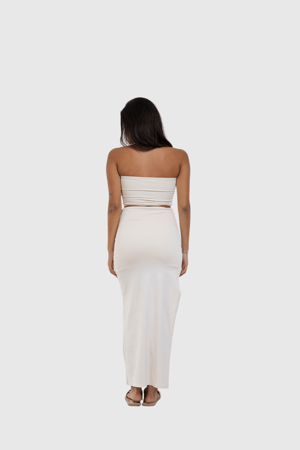 Modelo de costas vestindo saia midi off-white LA MAGIE com fenda, em poliamida justa que modela o corpo.