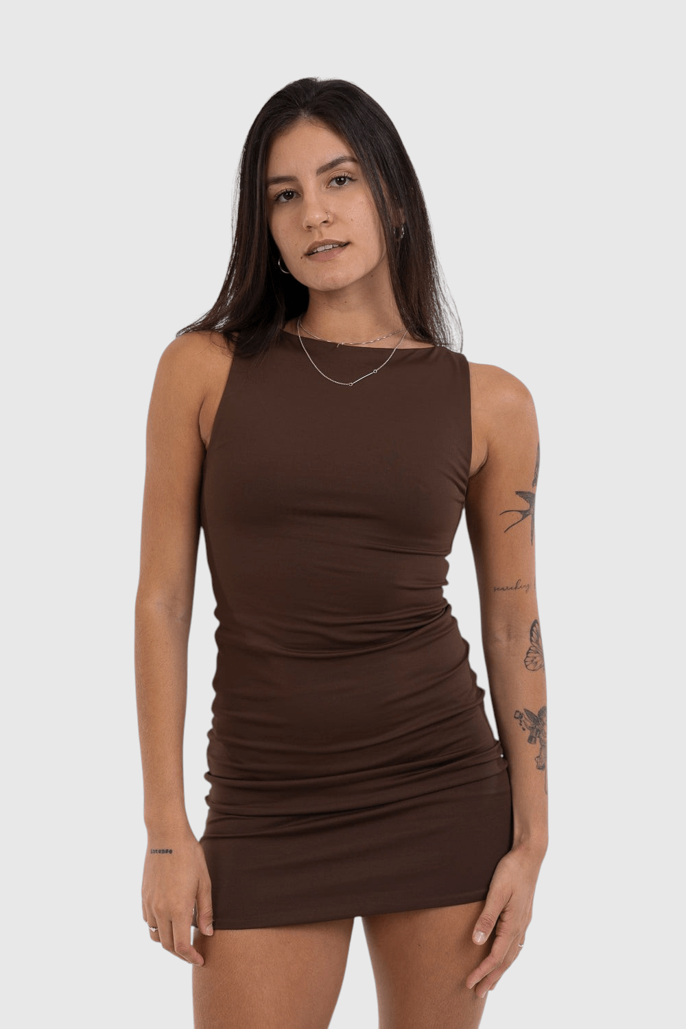 Modelo vestindo vestido curto marrom LA MAGIE em malha de poliamida com decote canoa e caimento ajustado ao corpo.
